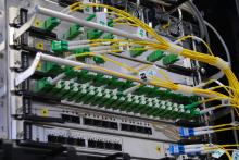 High-density fiber optic patch panel with green LC connectors and yellow fiber cables neatly organized in a server rack. This telecommunications infrastructure equipment illustrates the physical backbone that enables data transfer for both corporate IT systems and media production workflows.